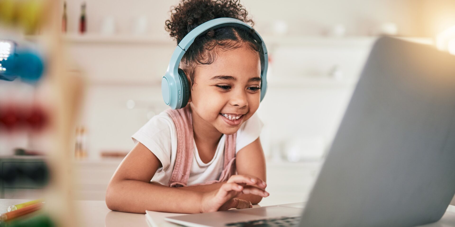 A cheerful girl wearing headphones uses a laptop, happily exploring online while staying safe from potential scams.