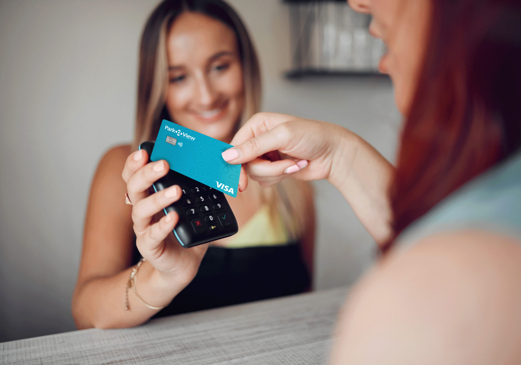 A woman happily holds a credit card, smiling. Using the tap to pay feature for a convenient and contactless transaction.