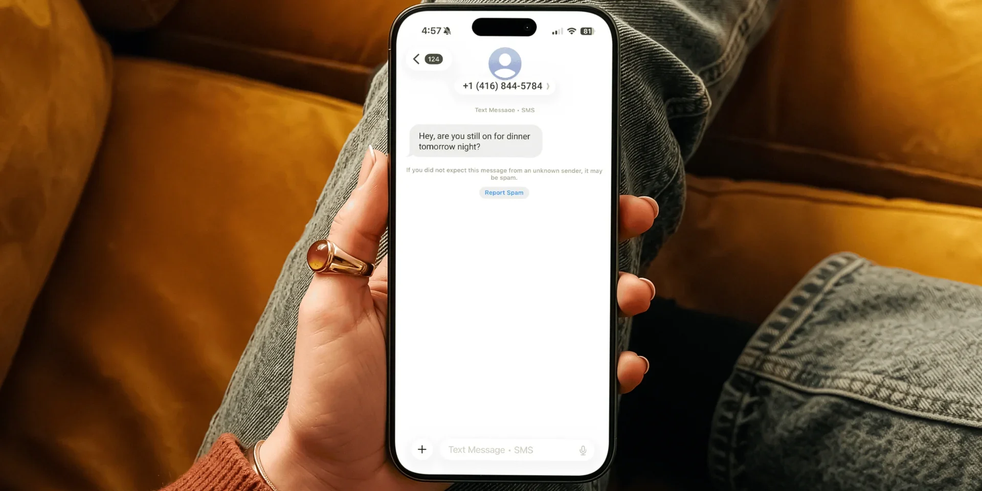 A person holding a smartphone displaying a wrong-number text message from an unknown sender asking about dinner plans that could be a scam.