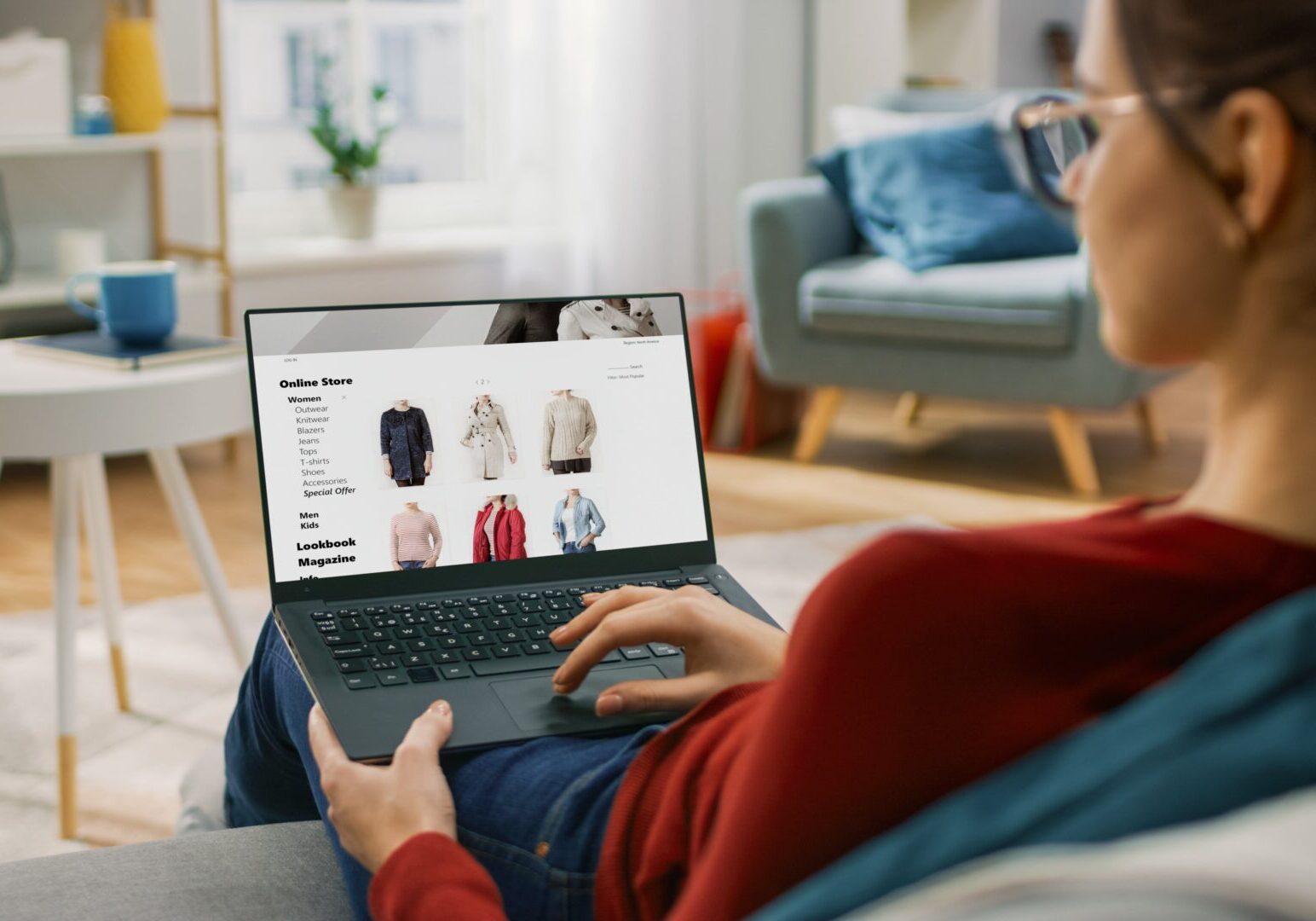 Young Woman at Home Using Laptop Computer for Browsing Through Online Retail Shopping Site. She's Sitting On a Couch in His Cozy Living Room. Over the Shoulder Camera Shot